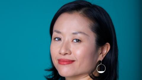 Yuko Miki turning and smiling at the photographer against a turquoise background